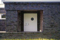 Überdachter Eingangsbereich im Klinkermauerwerk mit weißer Haustür und Bullauge