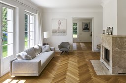 Großzügiges Wohnzimmer mit Natursteinkamin, Fischgrätparkett und bodentiefen Sprossenfenstern zum Garten