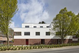 Straßenansicht des Mehrfamilienhauses mit Backsteinsockel, weißer Putzfassade und Staffelgeschoss