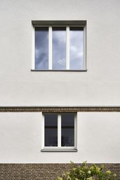 Fassadenausschnitt mit Klinkersockel, horizontalem Klinkergesims und weißen Holzfenstern