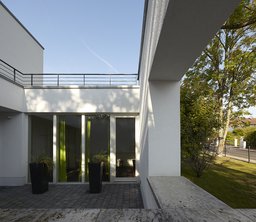 Geschützte Terrasse mit bodentiefen Fensterelementen, Pflasterbelag und kubischer Rahmung