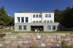 Gartenfassade mit grauem Sockelgeschoss, Loggia und vorgelagerter Natursteinmauer