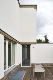 Geschützte Terrasse mit Holzdeck, Liegestuhl und Klinkergesims an weißer Putzfassade