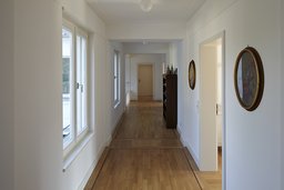 Heller Flur mit Parkettboden, dunklem Fries und seitlicher Fensterfront