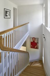 Lichtdurchfluteter Treppenraum mit Holzstufen, weißem Stabgeländer und Eichenhandlauf