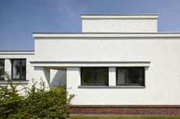 Weiße Putzfassade mit Flachdachstaffelung, Klinkersockel und dunklen Fensterprofilen