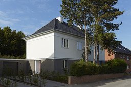 Straßenansicht des zweigeschossigen Wohnhauses mit Walmdach, dunklem Sockel und Garage