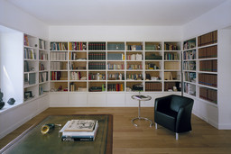 Großes Bibliothekszimmer mit wandfüllendem weißem Regaleinbau, Schreibtisch und Eichenparkett
