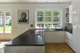 Moderne Küche mit dunkler Natursteinarbeitsplatte, weißem Sprossenfenster und Gartenblick