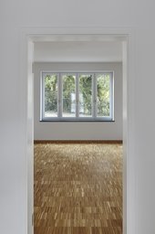 Blick durch Türöffnung in Wohnzimmer mit Stäbchenparkett und Fenster ins Grüne