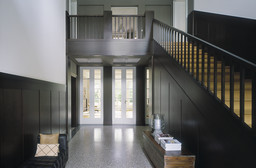 Großzügiges Foyer mit dunkler Holzvertäfelung, Terrazzoboden und Treppe zur Galerie