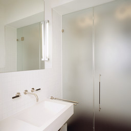 Minimalistisches Badezimmer mit weißem Blockwaschtisch, Wandarmaturen und satinierter Glastrennwand