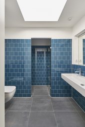 Modernes Badezimmer mit blauen Wandfliesen, Waschtisch, Dusche und zentralem Oberlicht