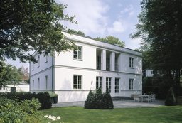Symmetrische Gartenfassade der weißen Villa mit Pfeilerloggia und gepflasterter Terrasse