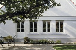 Gartenansicht mit weißer Putzfassade, profiliertem Gesimsband, Sprossenfenstern und kleiner Steintreppe