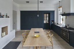 Großzügige Wohnküche mit dunkelblauen Einbauten, langem Holztisch und weißem Kamin