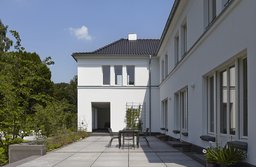 Gartenterrasse mit Plattenbelag und Sitzgruppe vor der weißen Putzfassade