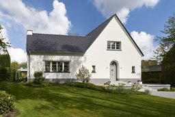 Straßenansicht mit weißer Putzfassade, steilem Satteldach und Hauseingang mit Rundbogen