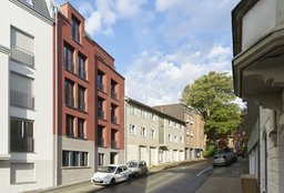 Straßenfassade des rot verputzten Mehrfamilienhauses mit Klinkersockel im städtebaulichen Kontext