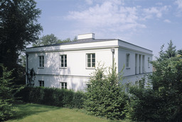 Eckansicht der zweigeschossigen weißen Villa mit Sprossenfenstern im eingewachsenen Garten