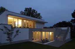 Gartenfassade in der Dämmerung mit erleuchteten Glasfronten, Außentreppe und Dachterrasse