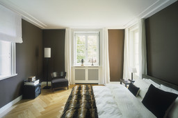 Elegantes Schlafzimmer mit dunkelbraunen Wänden, Fischgrätparkett und klassischer Heizkörperverkleidung