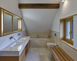 Badezimmer im Dachgeschoss mit Naturstein-Doppelwaschtisch, Einbauwanne und sichtbarem Deckenbalken