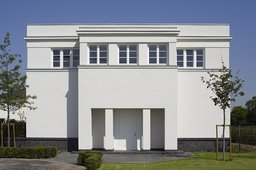Symmetrische Eingangsfassade mit markantem Risalit, überdachtem Pfeilerportal und klassischer Attika