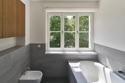 Modernes Badezimmer mit eingelassener Badewanne, grauen Fliesen und Sprossenfenster