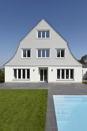 Symmetrische Giebelfassade mit heller Holzverschalung, Terrasse und Außenpool im Garten