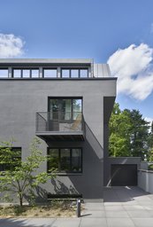 Grau verputzte Straßenfassade mit auskragendem Balkon, Gaubenband und seitlicher Garagenzufahrt