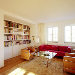 Wohnraum mit integrierter Wandbibliothek, Holzdielen, Sprossenfenstern und klassischer Sitzgruppe