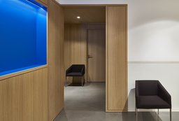 Flurbereich mit Holzverkleidung, blau beleuchteter Wandnische und anthrazitfarbenen Sesseln