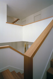 Mehrgeschossiges Treppenhaus mit weißen Brüstungswänden und massivem Holzhandlauf