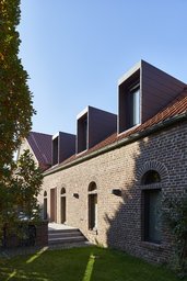 Historische Ziegelfassade mit Rundbogenfenstern und modernen kubischen Blechgauben