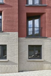 Fassadenausschnitt mit hellem Klinkersockel, dunklen Fenstern und rotem Besenstrichputz