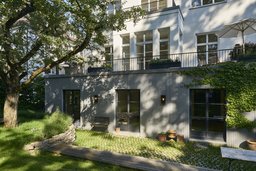 Gartenfassade mit grauem Sockelgeschoss, vorgelagerter Terrasse und bodentiefen Fenstertüren