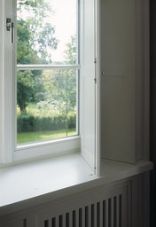 Weißer Innenklappladen in Laibung mit integrierter Heizkörperverkleidung und Gartenblick