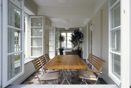 Lichtdurchflutete Veranda mit geöffneten Sprossenfenstern, gemustertem Fliesenboden und Holzesstisch