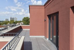 Großzügige Dachterrasse mit roter Putzfassade, Plattenbelag und weitem Ausblick