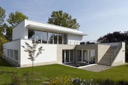 Gartenfassade mit Naturstein-Terrasse, Außentreppe zur Dachterrasse und bodentiefen Glasfronten