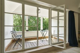 Überdachter Freisitz mit Holzbelag, Bistromöbeln und geöffneter weißer Sprossenfenstertür