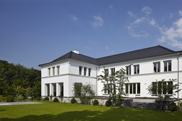 Gartenfassade des Einfamilienhauses mit Terrasse, dunklem Walmdach und Rasenfläche