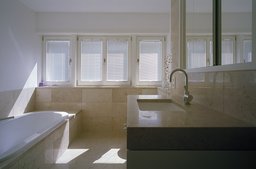 Lichtdurchflutetes Badezimmer mit hellem Naturstein-Waschtisch, eingelassener Badewanne und Fensterfront