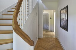 Helle Diele mit hellgrauer Holztreppe, geschwungenem Handlauf und Fischgrätparkett