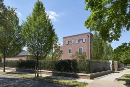 Straßenseitige Eckansicht der Backsteinvilla mit Klinkermauer und schmiedeeisernem Zaun