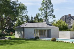 Poolhaus aus hellem Sandstein mit Walmdach und Swimmingpool im Garten