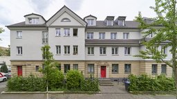 Sanierte Straßenfassade mit Werksteinsockel, Zwerchgiebel und roten Eingangstüren