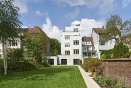 Gartenfassade des gestaffelten weißen Wohnhauses mit Weg und Backsteinmauer