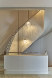 Geschwungene Treppe mit Edelstahlhandlauf und skulpturalen Glas-Pendelleuchten